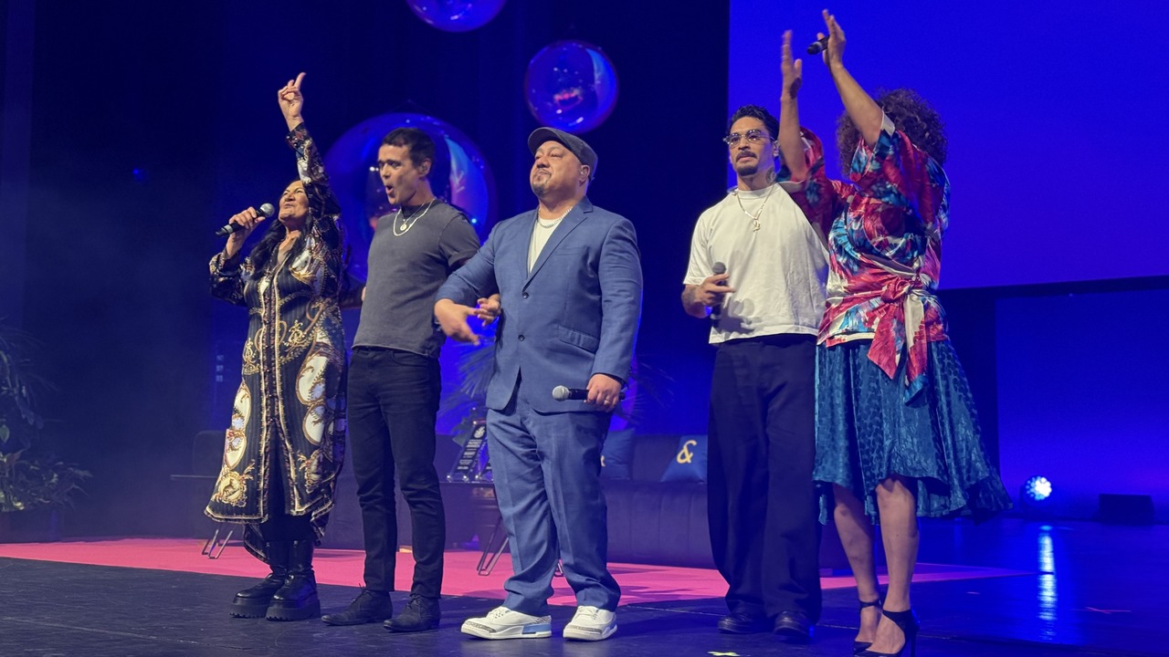 Five performers singing on stage with microphones under blue lighting at Summit 26
