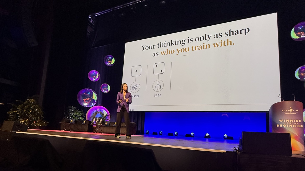 Keynote speaker Holly Ransom on stage at Summit 26 beside a slide reading Your thinking is only as sharp as who you train with