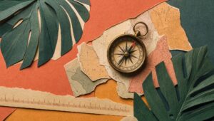 Hand-cut paper collage of a brass compass on torn mismatched map fragments framed by paper monstera leaves